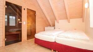 Una habitación de madera con una cama, un banco rojo y una puerta que da a un baño.