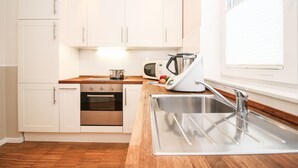 Una cocina moderna con armarios blancos, un lavamanos de acero inoxidable, un microondas y una tetera.