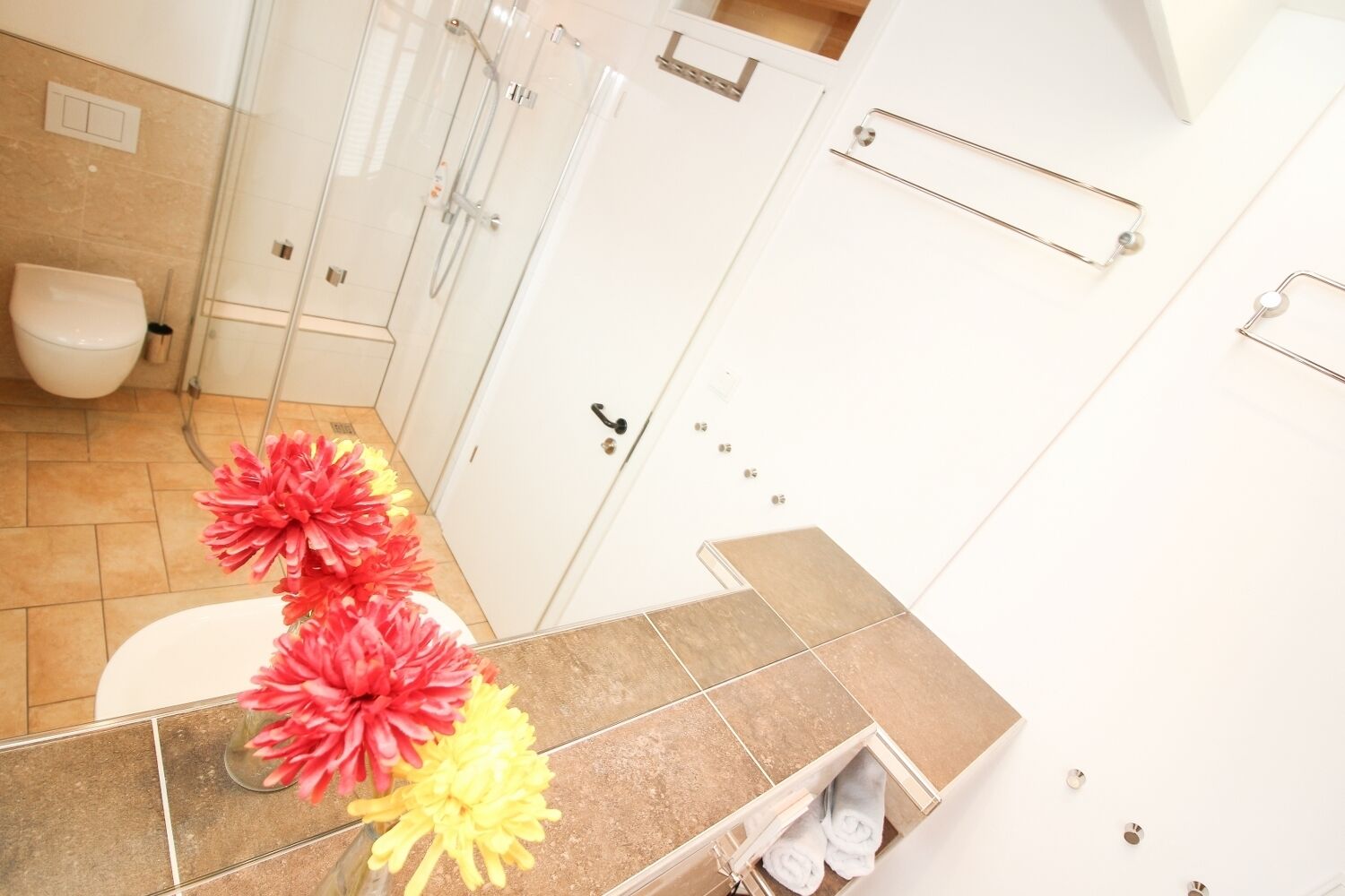 A bathroom with a toilet, shower, and sink. There are towels and a vase with flowers on the counter.