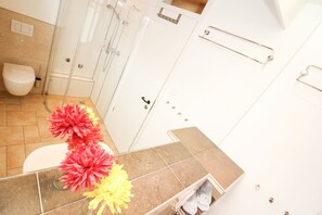 Un baño con inodoro, ducha y lavamanos. Hay toallas y un florero con flores sobre la encimera.