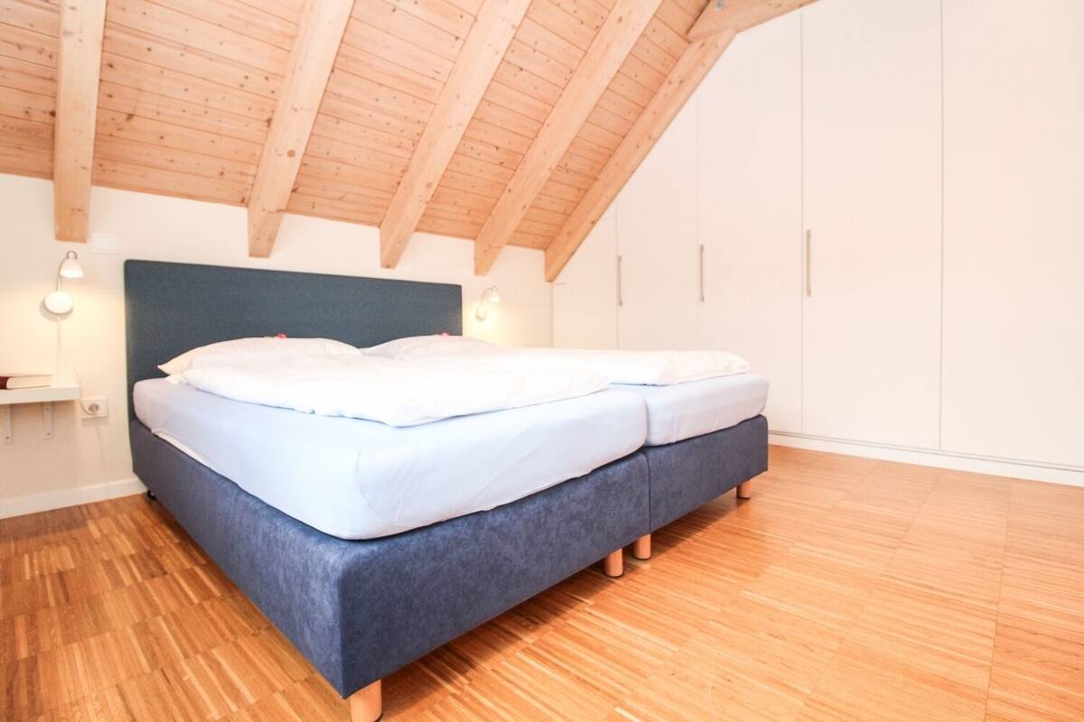 A bedroom with a bed, wooden floor, and a sloped ceiling.