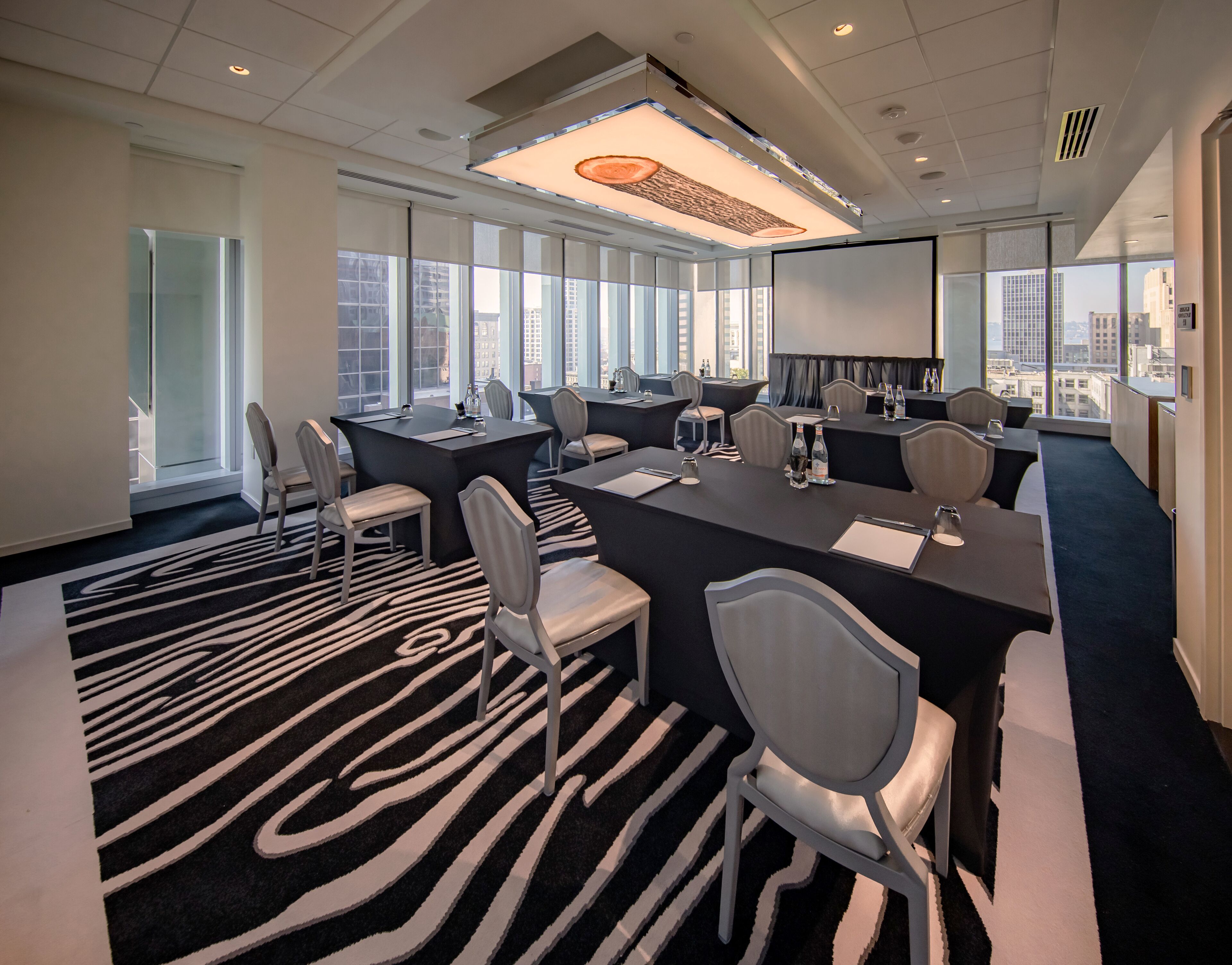 A modern conference room with a black and white zebra-patterned carpet, large windows offering city views, and a large screen for presentations.