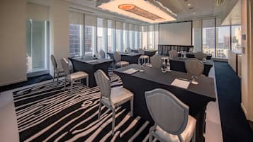 A modern conference room with a black and white zebra-patterned carpet, large windows offering city views, and a large screen for presentations.