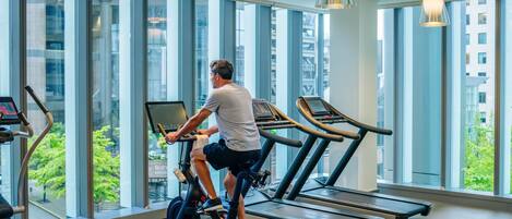 A gym with treadmills, exercise bikes, and large windows offering views of buildings and greenery.
