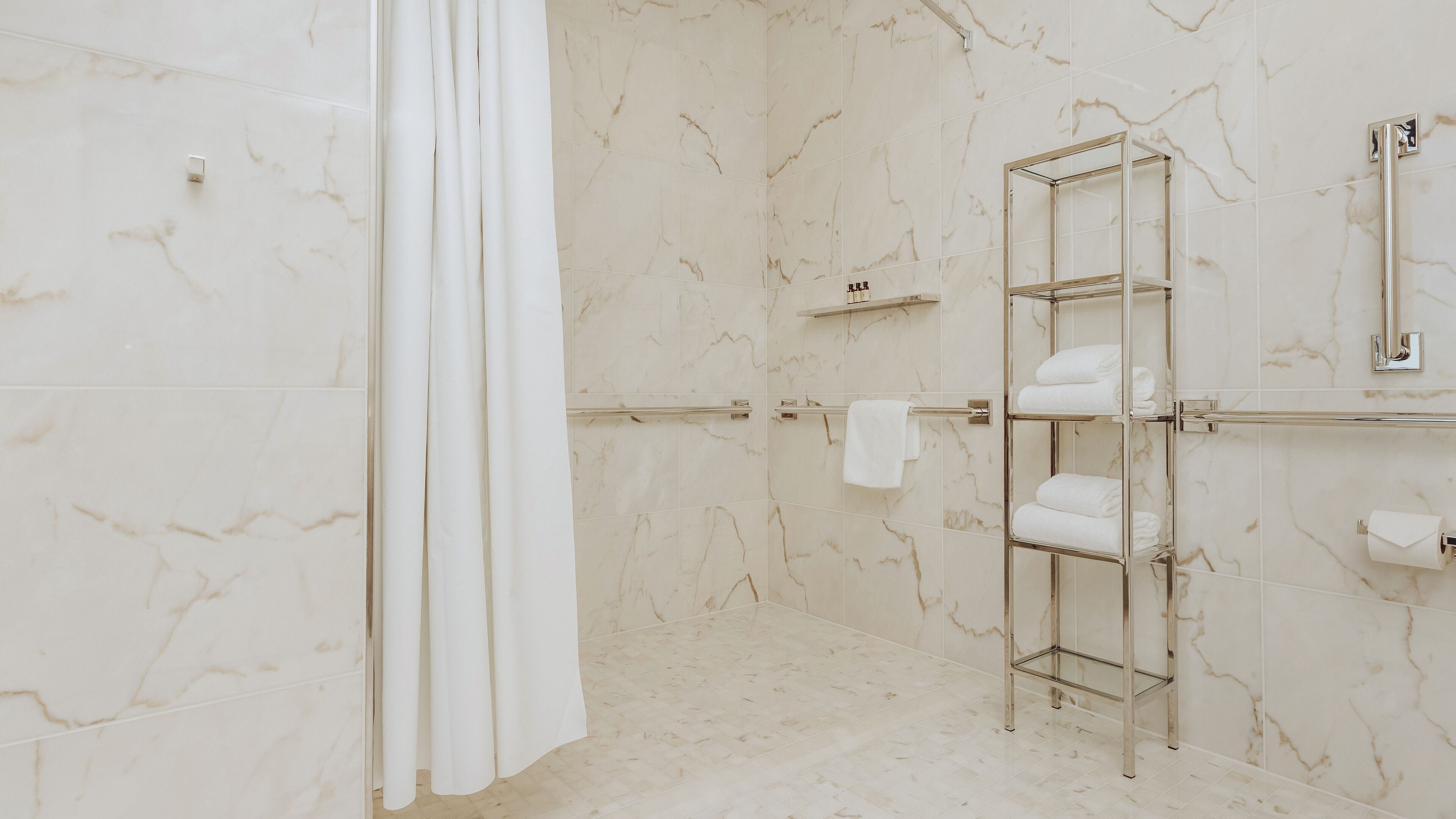A modern bathroom with marble walls, a glass shower enclosure, and a metal towel rack.