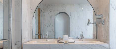 A modern bathroom with a large marble sink, dual faucets, and a large mirror.