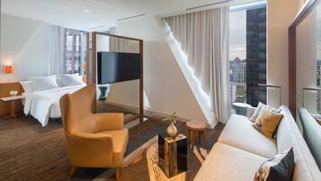 Een moderne hotelkamer met een bed, een bank, een stoel, een televisie en een balkon met gordijnen.