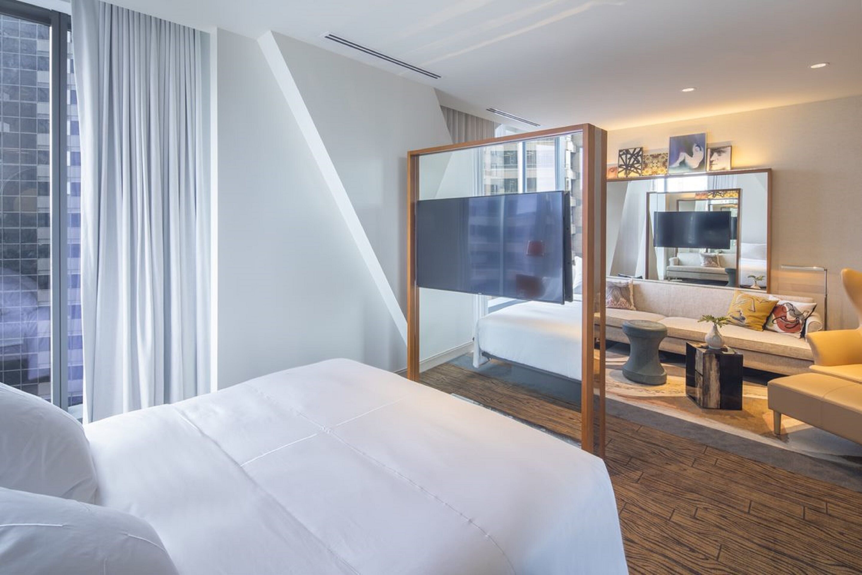 A modern hotel room with a large bed, a sofa, a TV, and a mirror.