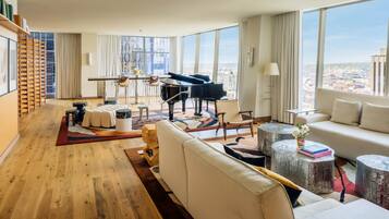 Un salón espacioso con un piano de cola, un sofá y vistas de la ciudad a través de amplios ventanales.