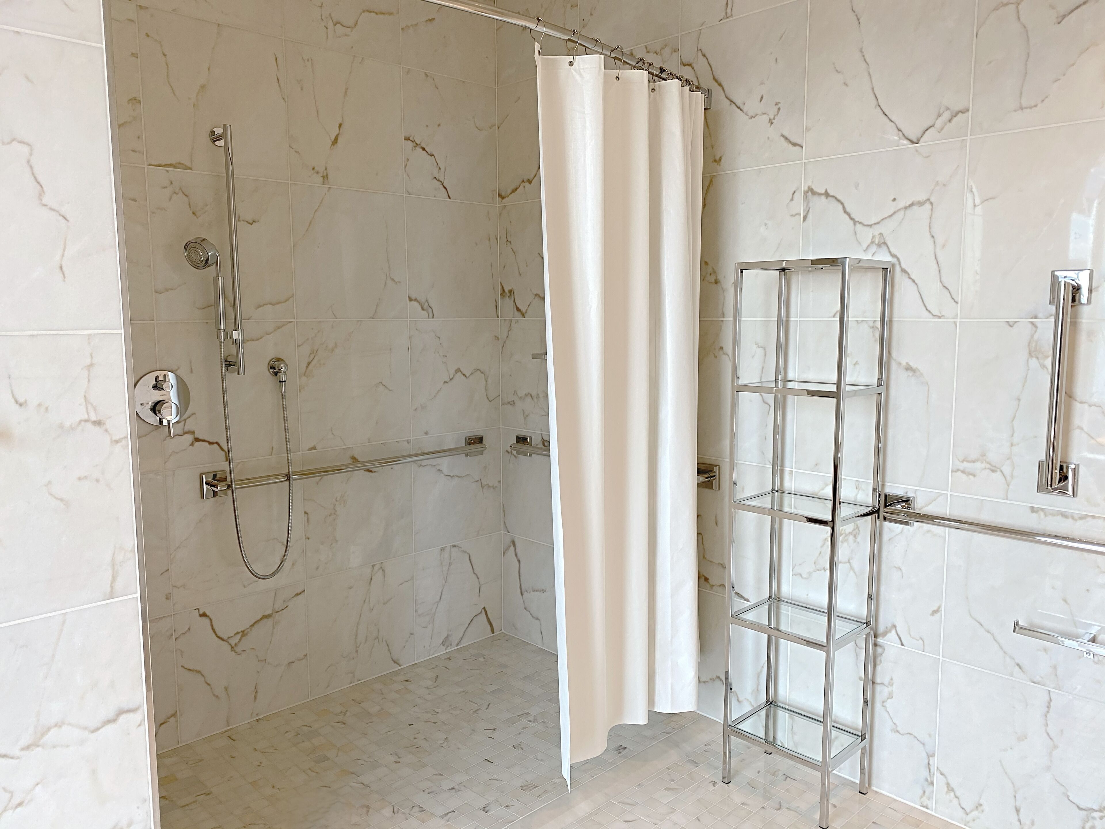 Een badkamer met een douche, een glazen plank en marmeren wanden.