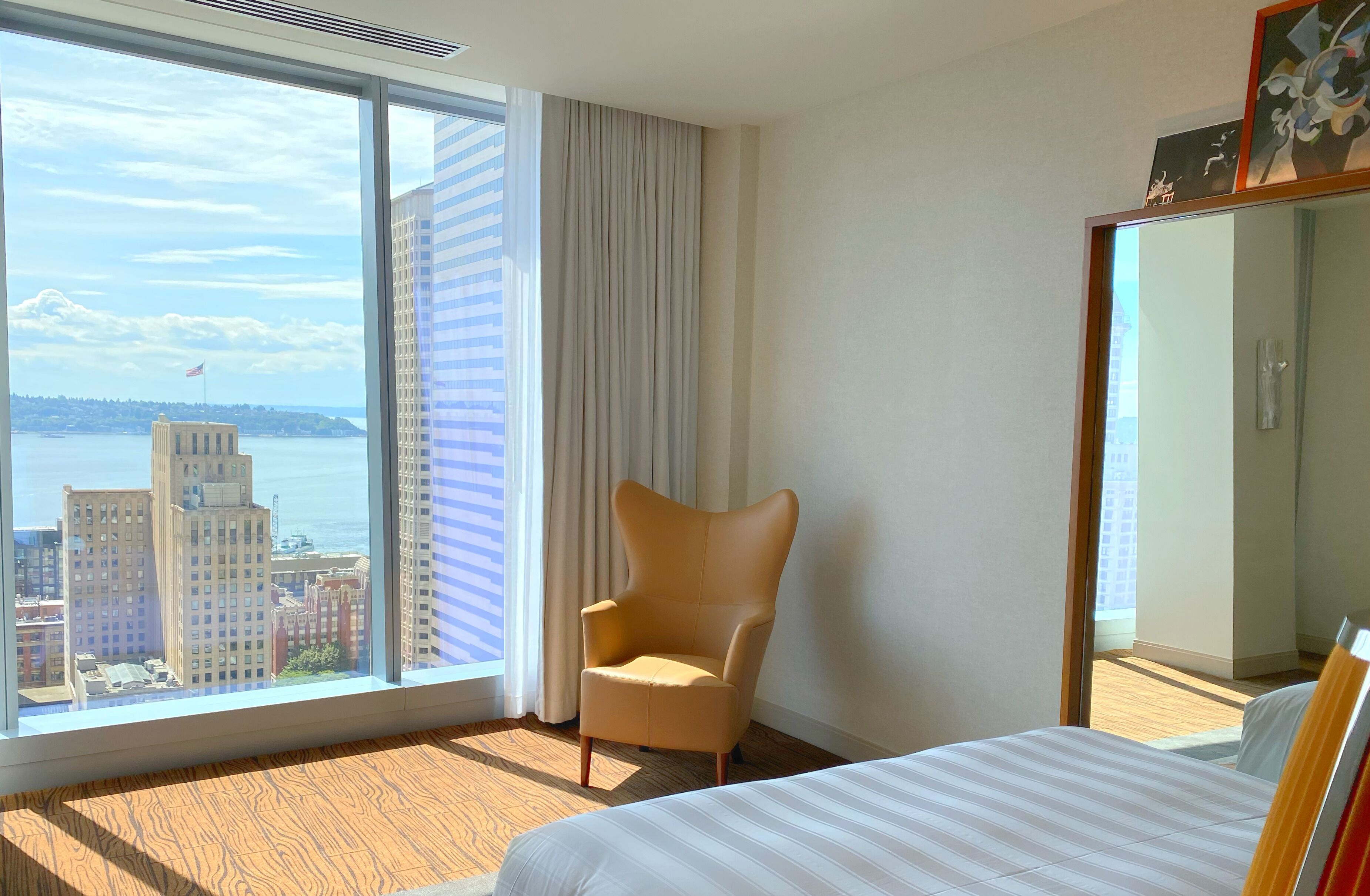 Habitación de hotel con un ventanal grande que ofrece vistas a la ciudad, una cama, un sillón y un armario.