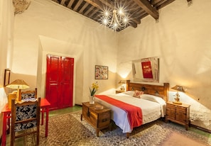Ein Schlafzimmer mit einem Bett, Holznachttischen, einer roten Tür und einer Kronleuchter.