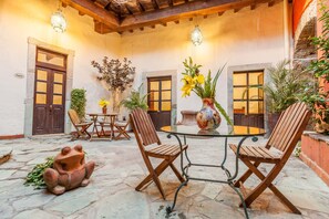 Un patio con una mesa redonda, dos sillas de madera, una maceta con forma de rana y plantas en macetas.