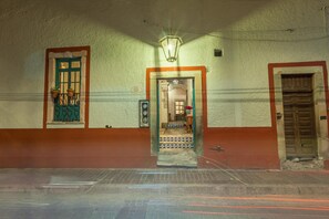 A hallway with a door leading to a room, a window with potted plants, and a wall-mounted light fixture.