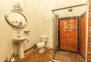 A bathroom with a white sink, a toilet, and a glass-enclosed shower area with orange and black tiles.
