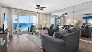 A spacious living room with a balcony, ceiling fans, and a large window with a view. - Beach Front, Balcony, Free Beach Chair Service, Tennis Pros (Miramar Beach)