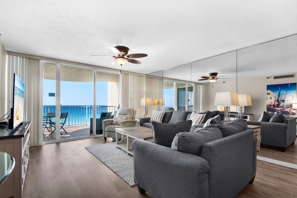A spacious living room with a balcony, ceiling fans, and a large window with a view. - Beach Front, Balcony, Free Beach Chair Service, Tennis Pros (Miramar Beach)