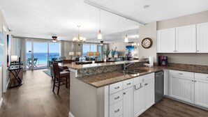 A modern kitchen with granite countertops, white cabinetry, and a dining area with a view of the ocean. - Beach Front, Balcony, Free Beach Chair Service, Tennis Pros (Miramar Beach)