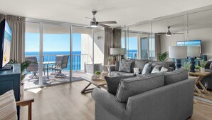 A modern living room with a grey sofa, a dining table, and a balcony with a view of the ocean. - Beach Front, Renovated Kitchen, Free Beach Chair Service (Miramar Beach)