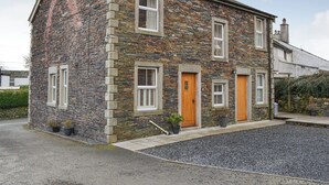 Une maison en pierre avec un toit en pente, une cheminée et une allée gravillonnée.