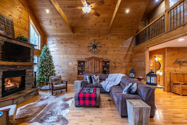 Interior acogedor de una cabaña de madera con chimenea, un árbol de Navidad, un amplio sofá de cuero y un rústico comedor.