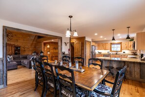 Un interior rústico con una mesa de comedor de madera, sillas y una zona de cocina con armarios de madera y encimera de granito.