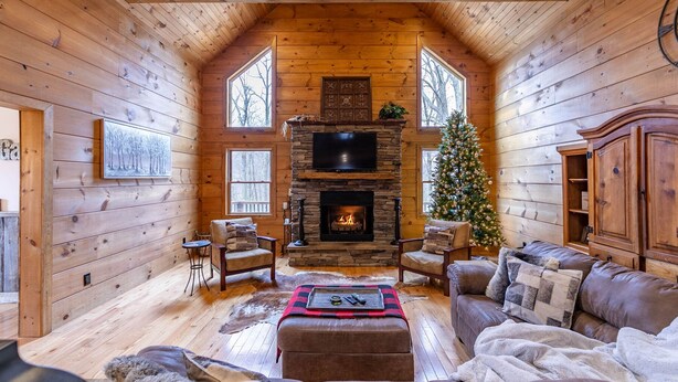 Interior acollidor d'una cabana de fusta amb una llar de pedra, mobles de cuir i un arbre de Nadal.