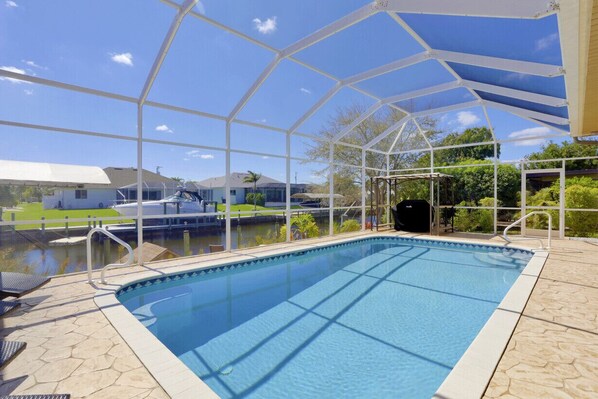 A swimming pool with a glass enclosure, surrounded by a patio area with lounge chairs.