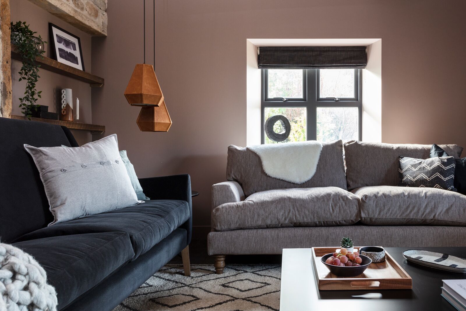 A modern living room with a dark blue sofa, a grey sofa, and a white coffee table with a fruit tray.