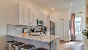 Een moderne keuken met witte kasten, een centraal eiland met krukken, roestvrijstalen apparatuur en een backsplash met een herringbone-patroon.