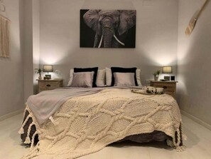 A bedroom with a large bed, a wall-mounted elephant artwork, bedside tables with lamps, and a textured blanket.