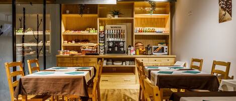 A cozy restaurant with wooden furniture, a central counter with a coffee machine, and shelves stocked with snacks and beverages.