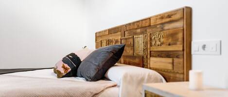 Una cama con cabecera de madera, una mesita de noche con cajón y una lámpara de pared.