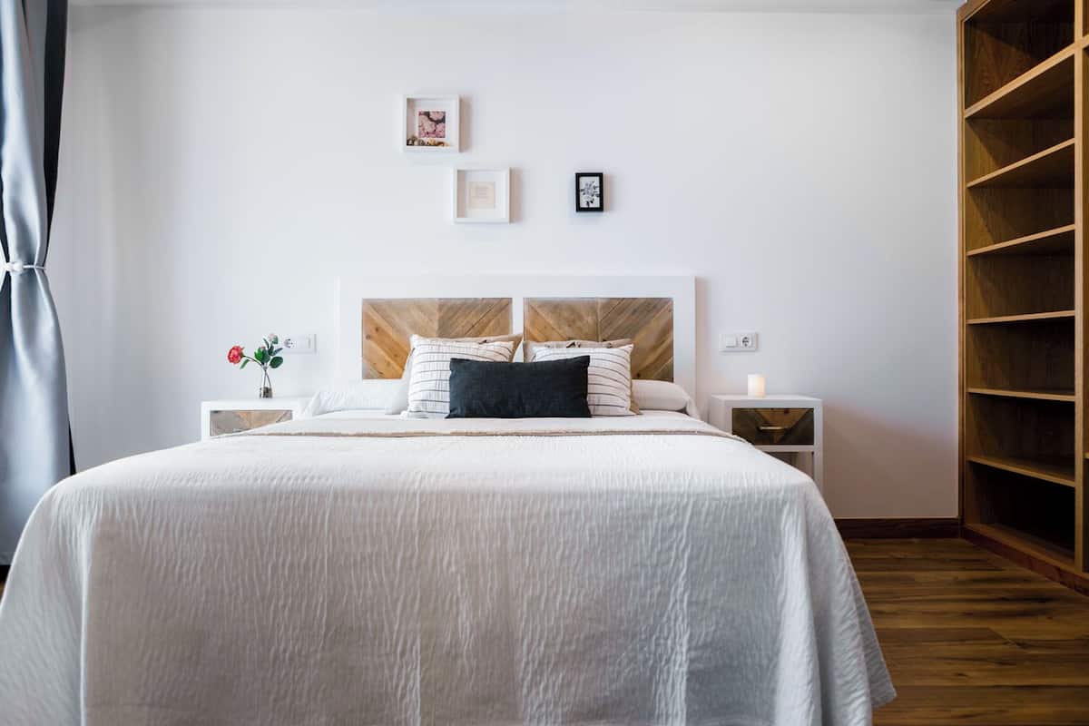 Ein ordentlich eingerichtetes Schlafzimmer mit einem großen Bett, zwei Nachttischen, einem Beistelltisch und einem Holzschrank.