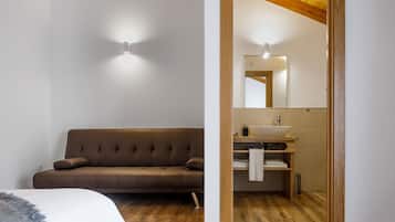 Un baño moderno con tocador de madera, un espejo grande y un sofá marrón en la habitación contigua.