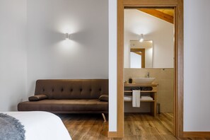 A modern bathroom with a wooden vanity, a large mirror, and a brown sofa in the adjacent room.