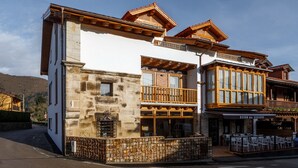 A multi-story building with a stone facade, wooden balconies, and a restaurant with outdoor seating. - Posada Rural Fuente Juliana (Ruente)