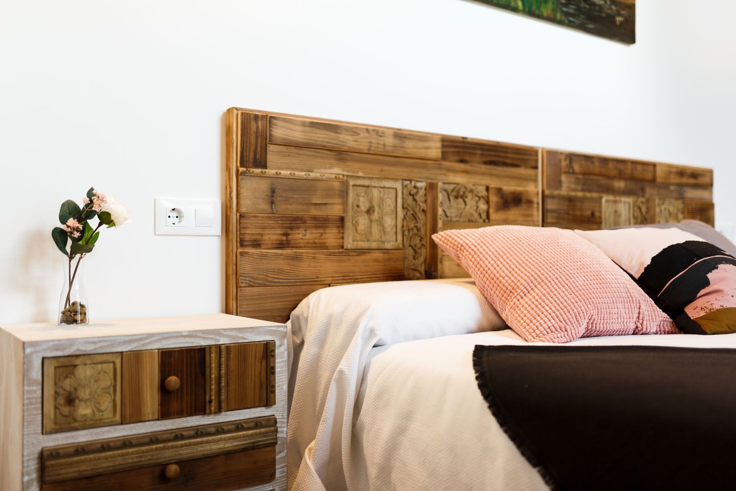 Un dormitorio con cabecera de madera, una mesita de noche con cajones y un jarrón con flores.