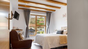 A bedroom with a bed, a chair, a TV, and a window with curtains. - Posada Rural Fuente Juliana (Ruente)