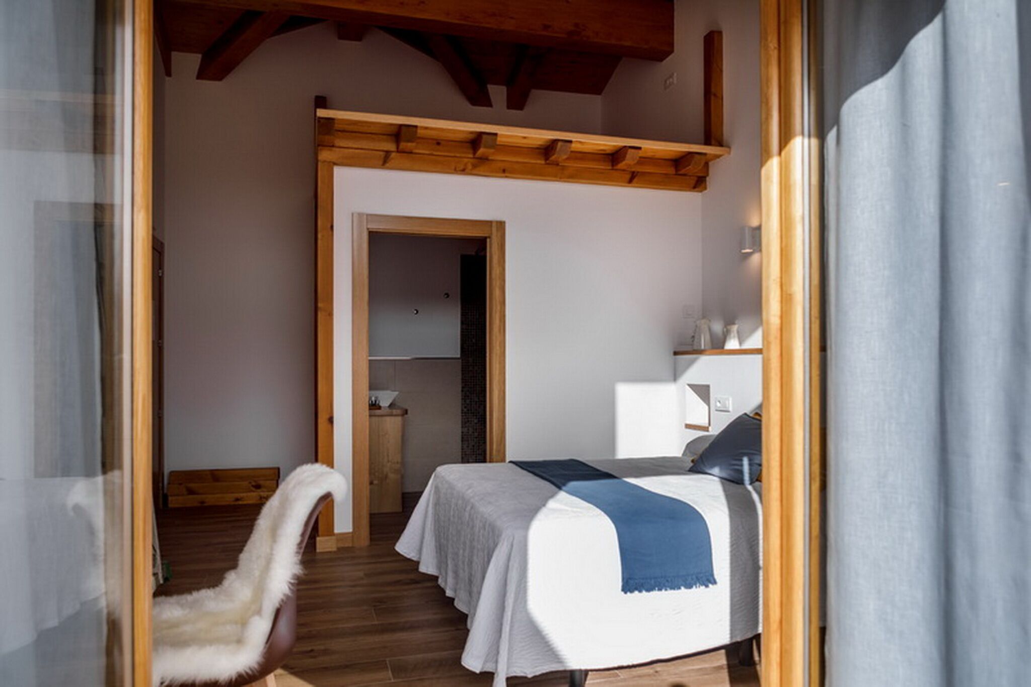 A bedroom with a bed, a chair, and a wooden ceiling.