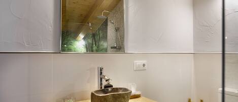 A bathroom with a wooden vanity, a stone sink, a glass of water, and a towel rack.
