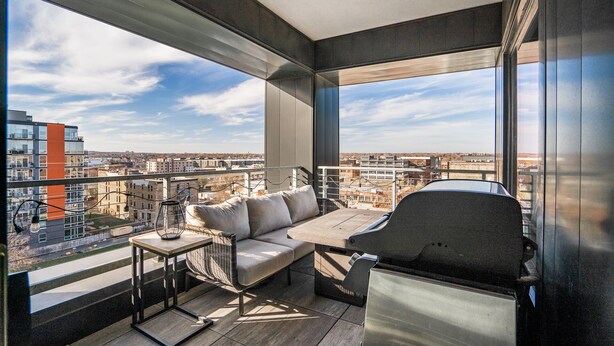 A balcony with a sofa, table, and grill, overlooking a cityscape. - MINNeSTAY* Sable 701 - Luxury Two Story Loft | North Loop | Target Center (Minneapolis)