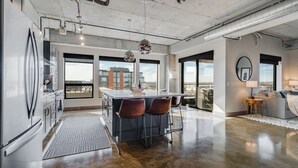 A modern kitchen with a bar area, large windows, and a view of the city. - MINNeSTAY* Sable 701 - Luxury Two Story Loft | North Loop | Target Center (Minneapolis)