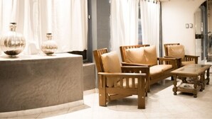 A modern lounge area with a sofa and chairs, a glass coffee table, and decorative vases on a marble counter. - Once Plaza Hotel (Buenos Aires)