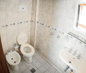 A bathroom with two toilets, a bidet, a sink, and a mirror. - Once Plaza Hotel (Buenos Aires)