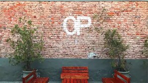 A brick wall with a white 'CP' graffiti, three wooden benches, and two potted plants. - Once Plaza Hotel (Buenos Aires)