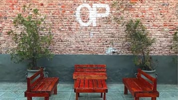 Un muro de ladrillo con grafiti blanco que dice 'CP', tres bancos de madera y dos plantas en macetas.