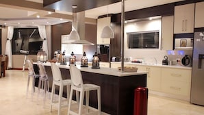 Une cuisine moderne dotée d’un îlot central, de tabourets de bar, de luminaires suspendus et d’un réfrigérateur en acier inoxydable.