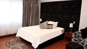 Une chambre à coucher avec un grand lit, une tête de lit dotée de lampes, une table de chevet, un fauteuil à motifs et un tapis en fourrure.