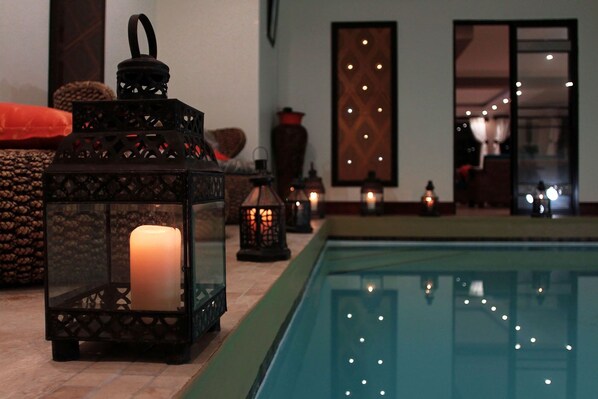 A pool area with a candle in a lantern, surrounded by other lanterns and a patterned wall.